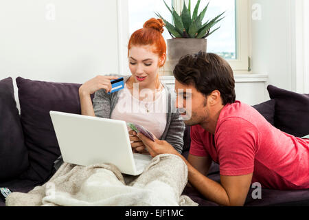 Close up molto felice coppia giovane con Laptop seduta sul lettino e gettare denaro euro nell'aria. Foto Stock