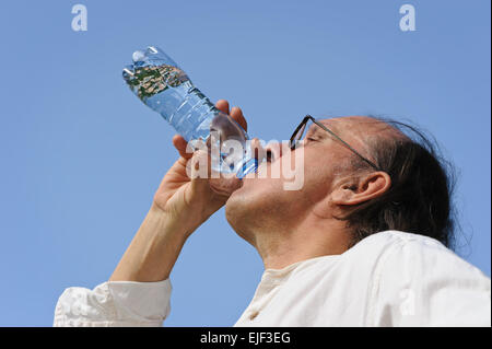 Sete senior uomo beve l'acqua da una bottiglia all'esterno. C'è un lago e la foresta in background. Bassa angolazione della telecamera. Foto Stock