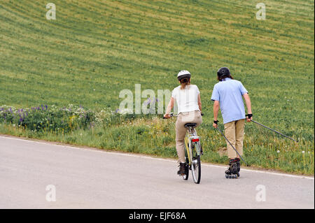 Coppia senior vigorosamente esercizio. L'uomo è nordico pattinaggio inline e la donna è in bicicletta. Foto Stock