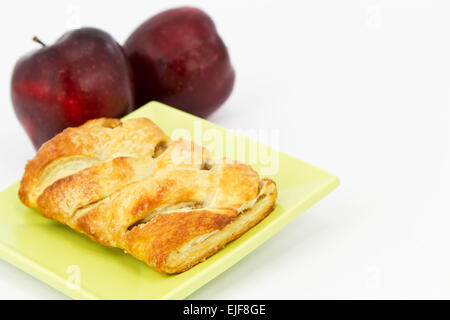 Cotta strudel di mele sulla luce piastra di verde con 2 mele rosse dietro. L'immagine orizzontale con copia in bianco lo spazio. Foto Stock