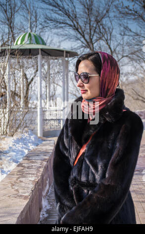Una donna in occhiali da sole che indossa un nero pelliccia appare in lontananza Foto Stock
