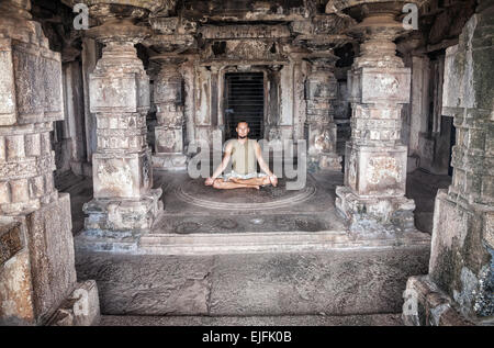 Uomo che fa la meditazione in antico tempio con colonne di carving in Hampi, Karnataka, India Foto Stock