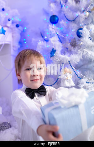 Little Boy in una camicia bianca ed il filtro bow tie decora un albero di Natale Foto Stock