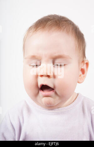Ritratto di otto mesi di età adorabile bionda simpatico baby pink velvet onesie disgustato o starnuto faccia isolato su bianco Foto Stock