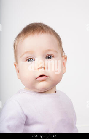 Ritratto di otto mesi di età adorabile bionda simpatico baby pink velvet onesie guardando il volto della telecamera isolato su bianco Foto Stock