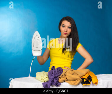 Houseworks, donna con il mucchio di vestiti per la stiratura, su sfondo blu Foto Stock