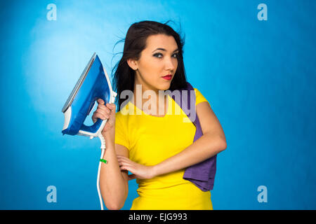 Houseworks, donna con il mucchio di vestiti per la stiratura, su sfondo blu Foto Stock