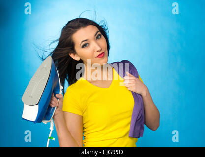 Houseworks, donna con il mucchio di vestiti per la stiratura, su sfondo blu Foto Stock