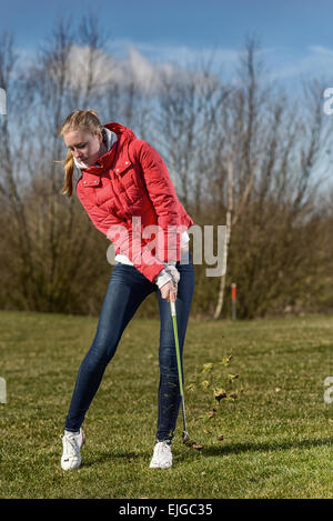 A piena lunghezza shot di un giovane giocatore di golf femminile, indossa una giacca rossa e Skinny Jeans, nella ruvida, appena dopo aver disputato una sfera Foto Stock