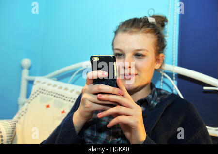 Ragazza adolescente controlli di facebook e twitter sul suo telefono cellulare nella sua camera da letto Foto Stock
