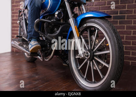 Uomo a cavallo di un blu moto sportiva sulla casa pavimento in legno, sottolineando la ruota in stretta verso l'alto. Foto Stock