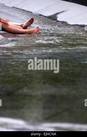 Due persone il raffreddamento gambe e piedi in Princess Diana's Memorial Fontana, Hyde Park, Londra, Inghilterra Foto Stock