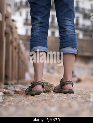 Vista posteriore di una donna per le gambe in piedi sulla spiaggia di ciottoli, Hastings, Regno Unito Foto Stock