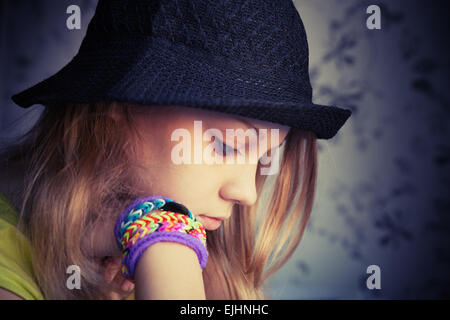 Ritratto di profilo di bella bionda ragazza adolescente in black hat e telaio in gomma braccialetti, vintage tono scuro foto, instagram sty Foto Stock