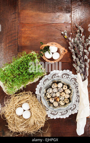 Composizione di pasqua di rametti di salice con ramoscelli, crescione, uova di quaglia in piatto metallico, paglia nido e cesto di pasqua, sul tavolo Foto Stock