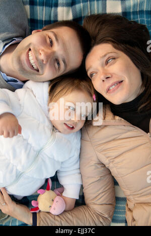 Madre padre e la loro figlia piccola avente tempi felici insieme in autunno per esterno in legno verde e di erba Foto Stock