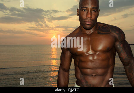 Silhouette di un culturista che pongono al tramonto sulla spiaggia, formazione al mattino, uomo forte che mostra i suoi muscoli Foto Stock