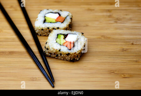 Il riso sushi con nori, salmone, pesce bianco e avocado avvolti all'interno di seduta su una scheda di bambù con bacchette nere Foto Stock
