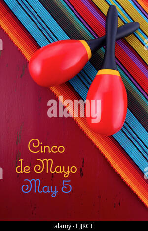 Happy Cinco de Mayo sfondo con le maracas in stile messicano sul tessuto rosso invecchiato in legno tavolo. Foto Stock