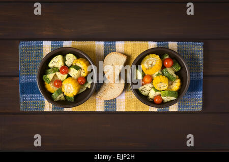 Tettuccio di colpo di due ciotole di verdura cotta di mais dolce, zucchine, pomodori ciliegia con il timo, fette biscottate accanto Foto Stock