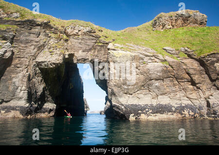 Sea kayaker passando attraverso un arco di roccia nei pressi del porto, County Donegal, Irlanda. Foto Stock