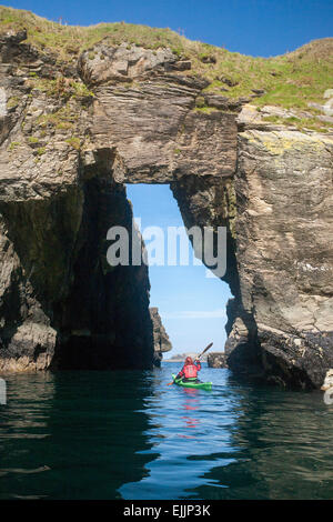 Sea kayaker passando attraverso un arco di roccia nei pressi del porto, County Donegal, Irlanda. Foto Stock
