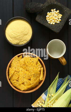 Tettuccio di colpo di tortilla chips in ciotola di legno circondato dai suoi ingredienti acqua e farina di mais e grano, fotografato in legno scuro Foto Stock