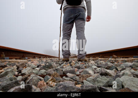 Un uomo a camminare sulle vie con la canna da zucchero e trekking i vestiti di una fitta giornata di nebbia Foto Stock