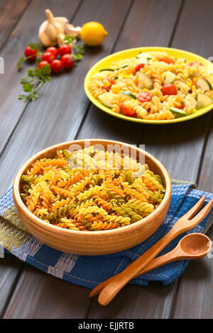 Materie tricolore fusilli o pasta rotini (tradizionale, pomodoro e spinaci gusto) nella ciotola di legno con insalata di pasta e gli ingredienti Foto Stock