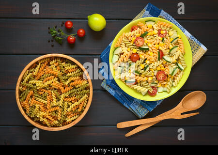 Colpo di overhead di materie fusilli nella ciotola di legno e un piatto di pasta vegetariana insalata Foto Stock