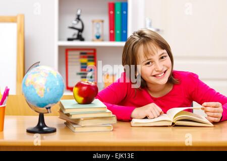 Piuttosto schoolgirl lettura in Aula. Globo terrestre e tutta la apple su altri libri impilati Foto Stock