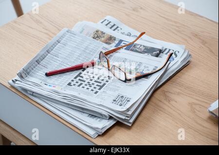 Una selezione di quotidiani su un tavolino con penna cruciverba e bicchieri Foto Stock