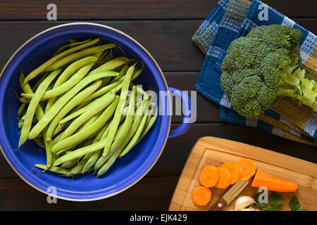 Tettuccio di colpo di fagioli verdi in blu il filtro di metallo con broccoli e tagliare la carota sul lato, fotografato in legno scuro Foto Stock