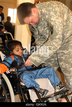 Capitano Seth Palmer si inserisce Mustafa Murtah, 5, con un nuovissimo carrozzella dic. 13 presso il Palazzo Radwaniyah complesse operazioni Civili-Military Center. Quindici bambini ricevuto carrozzina donati a carrozzine per bambini iracheni. Foto Stock