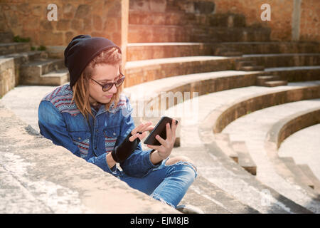 Libero professionista ragazzo con dreadlocks seduti sulla scalinata con tavoletta digitale digitando messaggio caldo filtro applicato Foto Stock