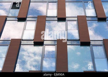 Blu cielo coperto da nuvole e nuvole riflettono in specchio finestre del nuovo ufficio moderno edificio con una sezione aperta Foto Stock