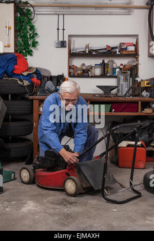 Lavoratori anziani mantenendo il suo tosaerba in officina. Foto Stock