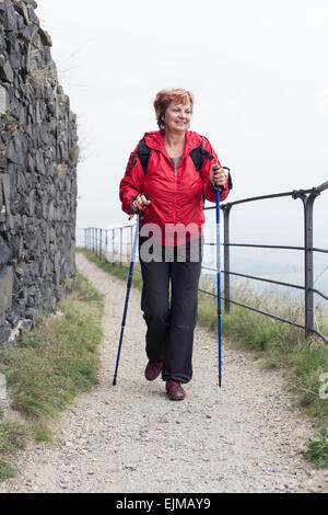 Attiva donna senior Nordic walking sul sentiero roccioso all'esterno. Foto Stock