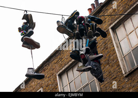 Alcune vecchie sneakers appendere su un filo di telefono contro un cielo bianco in South London REGNO UNITO Foto Stock