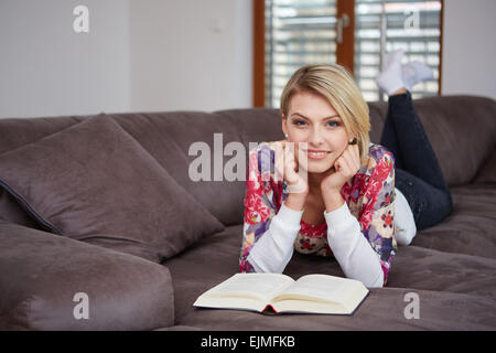 Donna godendo la lettura di un libro a casa sdraiato sul divano Foto Stock