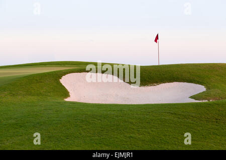 Bandiera rossa del golf foro sopra sabbia trappola o bunker sul bellissimo campo al tramonto Foto Stock