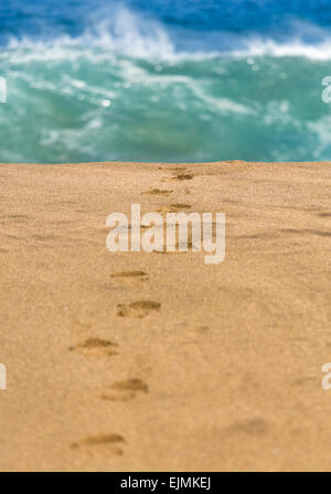 Liscia e spiaggia di sabbia con orme uno che conduce verso le onde che si infrangono nella distanza Foto Stock