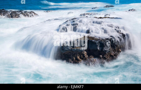 Forti onde del mare il flusso sulle rocce laviche sul bordo della spiaggia vicino al Queens bagno, Kauai, Hawaii Foto Stock