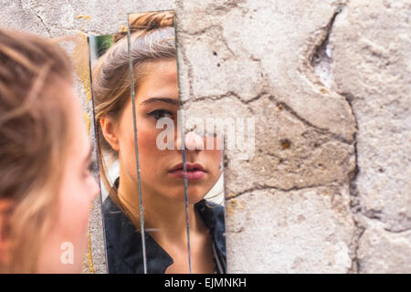 Teen ragazza guardando il suo riflesso in frammenti di specchio sulla parete a street. Foto Stock