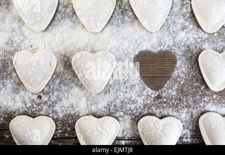 Ravioli di greggio in forma di cuori, cospargere di farina, su sfondo di legno closeup. Gnocchi di cottura. Vista dall'alto. Foto Stock