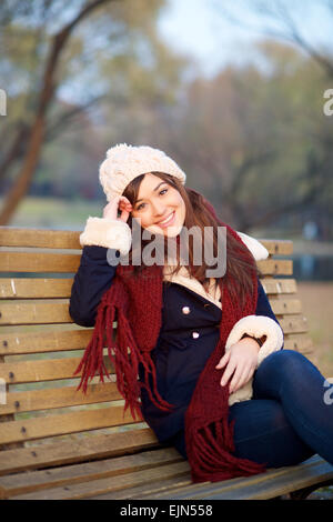 Ragazza seduta sulla panchina nel parco in inverno guardando la fotocamera Foto Stock