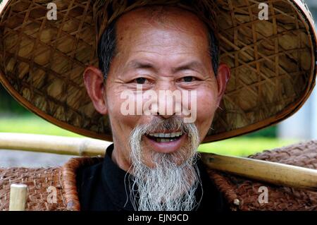 Yangshuo, Cina: Cinese sorridente "bird l uomo di Yanshuo indossando un cappello di paglia con un palo di bambù in appoggio sulla sua spalla Foto Stock