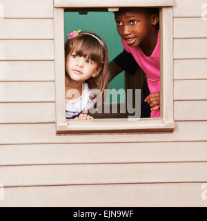 Due ragazze che giocano insieme in una playhouse e guardando attraverso la finestra Foto Stock