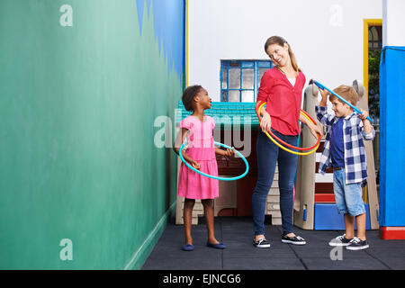 I bambini e l'asilo nido insegnante con hula hoops in kindergarten Foto Stock