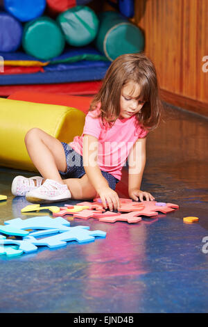 Ragazza risolvere un grande puzzle sul pavimento in un kindergarten Foto Stock